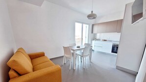 A modern living room with a sofa, a dining table with chairs, a kitchen area with cabinets and appliances, and a large window. - Air-conditioned apartment with sea view terrace - Santa Maria Castellabate (Castellabate)
