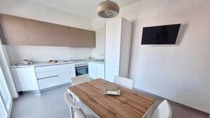 A modern kitchen with white cabinets, a wooden dining table, and white chairs. - Air-conditioned apartment with sea view terrace - Santa Maria Castellabate (Castellabate)