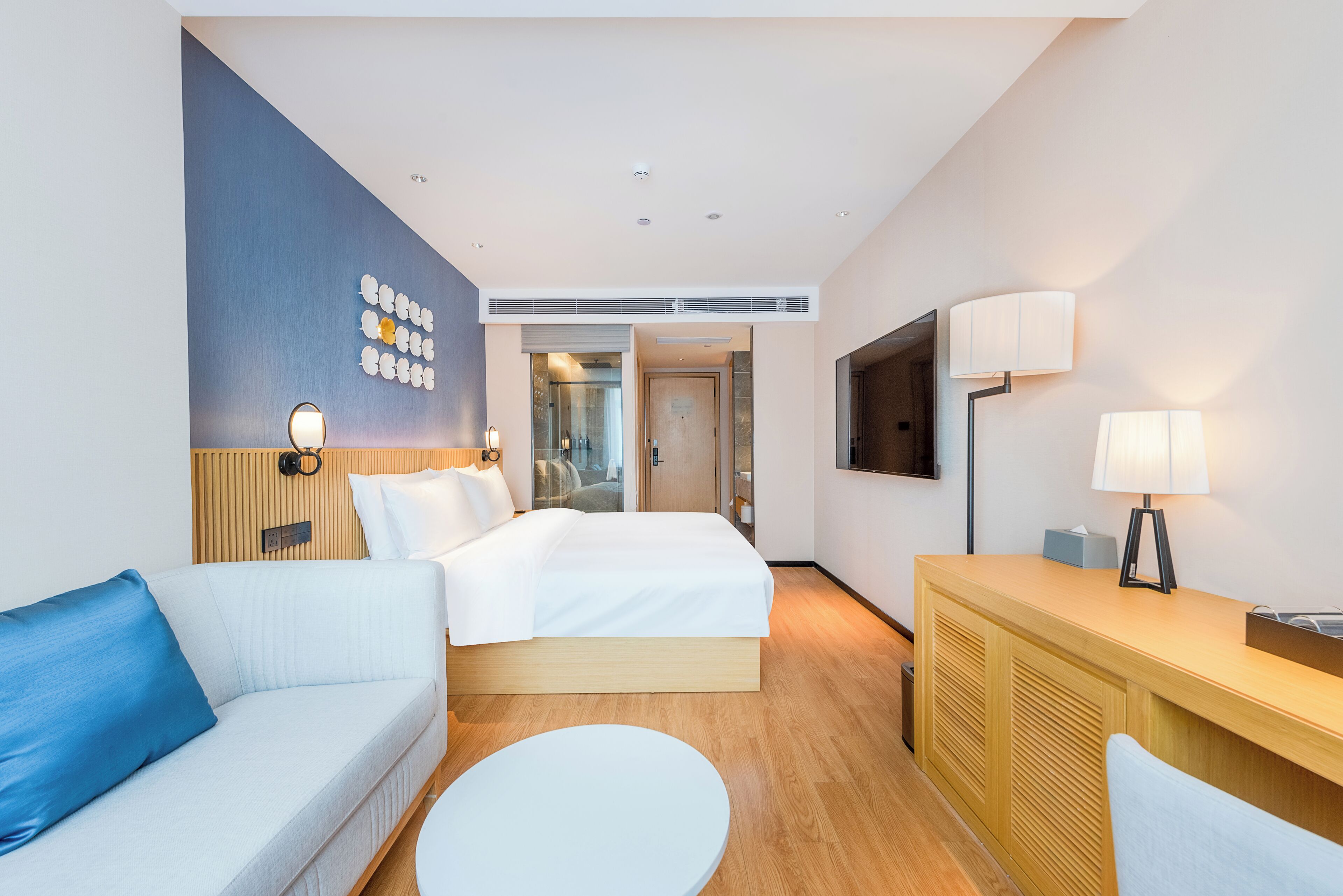 A hotel room with a bed, a sofa, a desk, a TV, and a wall with decorative items.