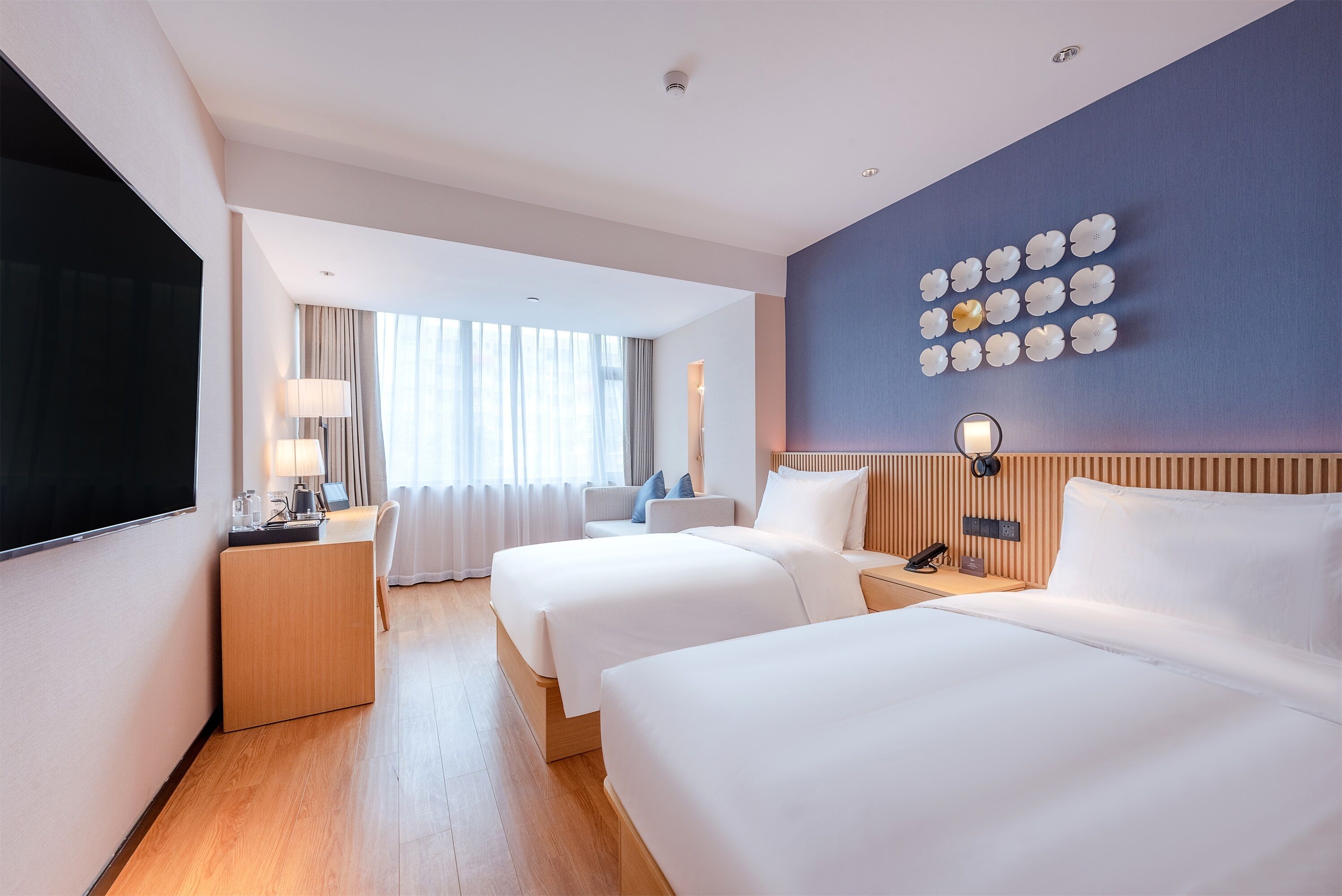 A hotel room with two beds, a desk, a TV, and a wall with decorative plates.