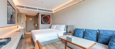 A modern hotel room with a bed, a sofa, a desk, and a wall-mounted TV.