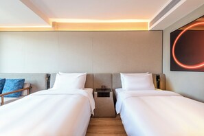 Habitación de hotel con dos camas, una mesita de noche, un banco de madera y una lámpara circular fijada a la pared.