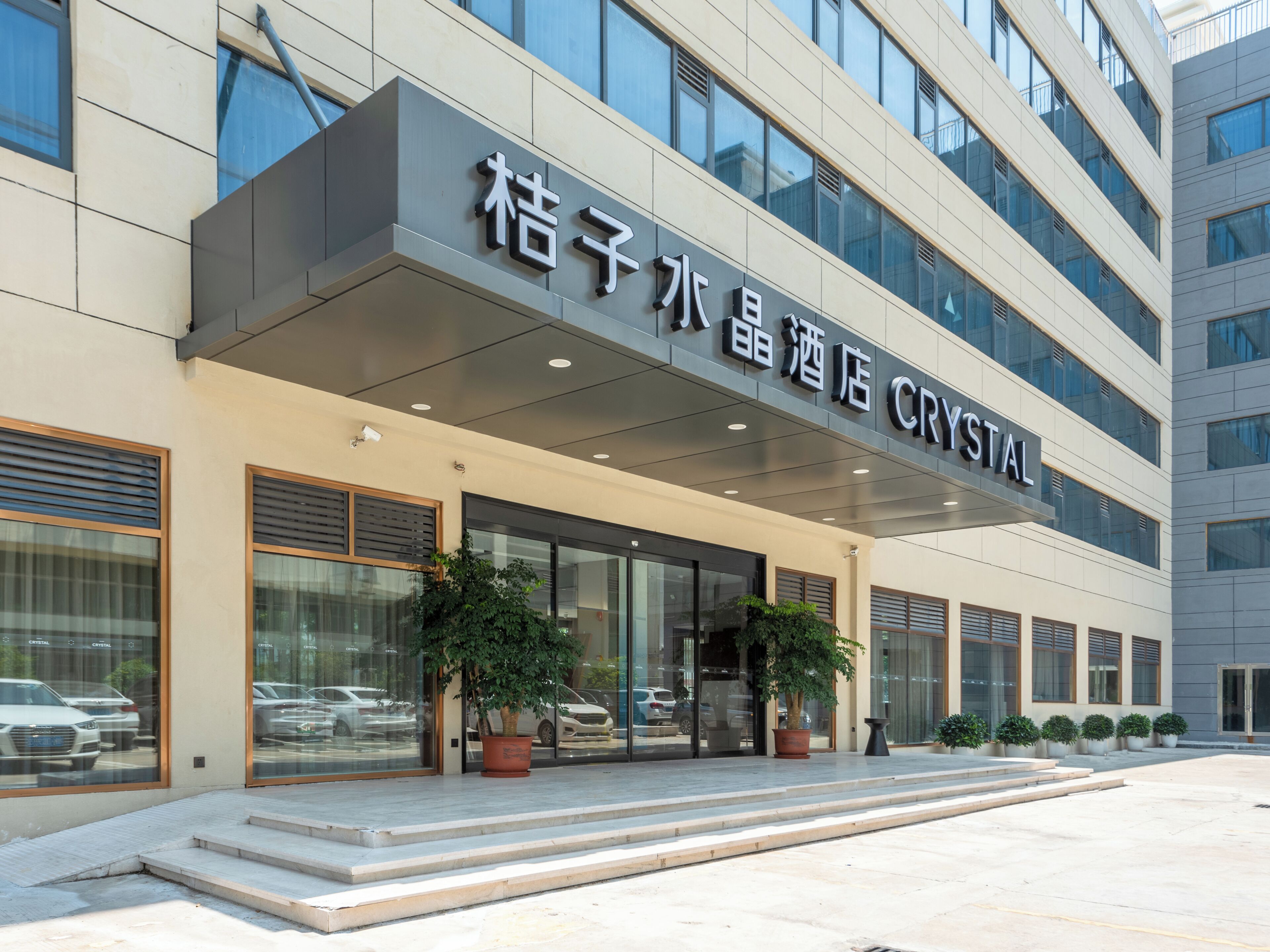 A hotel entrance with a modern facade, large windows, and potted plants.