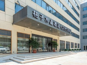 A hotel entrance with a modern facade, large windows, and potted plants. - Crystal Hotel Huafa Ice and Snow World (Shenzhen)