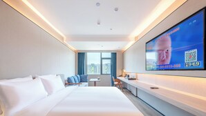 Habitación de hotel con una cama grande, un escritorio, una silla, un televisor en la pared y una ventana con cortinas.
