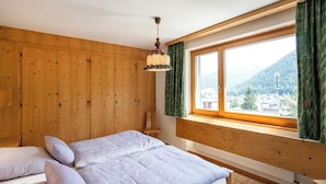 Une chambre avec un lit superposé en bois, une fenêtre donnant sur une ville et des montagnes, et un luminaire suspendu.