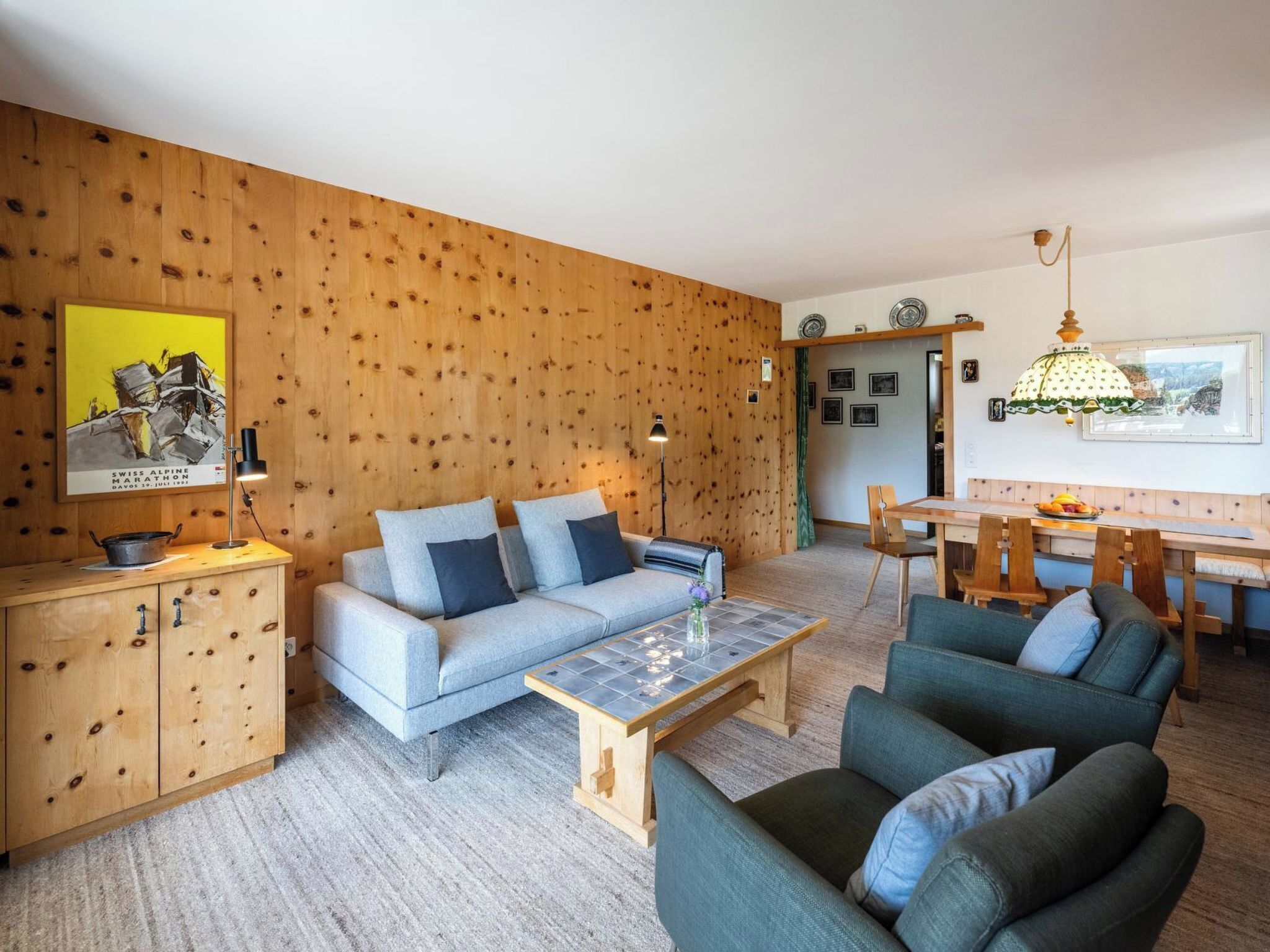 Uma sala de estar com sofá, poltronas, mesa de centro e uma área de jantar com mesa e cadeiras.