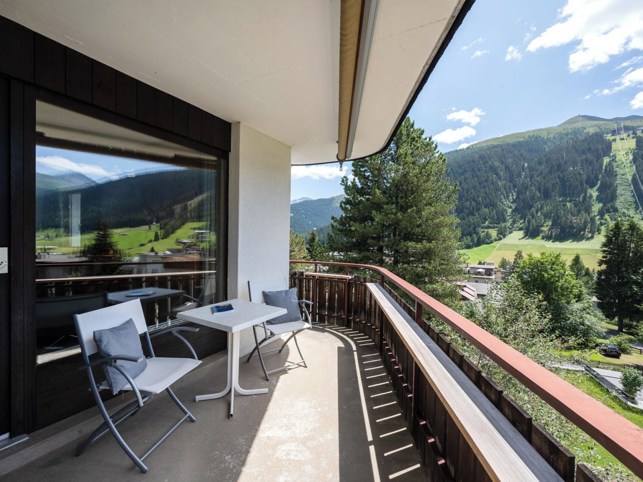 Een balkon met een tafel en stoelen, uitzicht op een bergachtig landschap en een houten hekwerk.