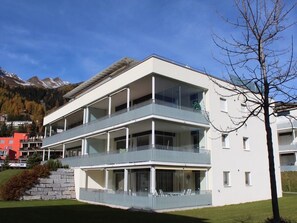 Ein modernes, mehrstöckiges Gebäude mit Balkonen, großen Fenstern und Blick auf Berge im Hintergrund.