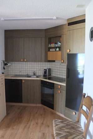 Una cocina compacta con armarios de madera, microondas integrado y refrigerador.