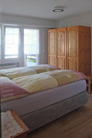 Un dormitorio con cama, armario de madera y ventana con cortinas.