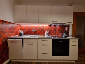 Eine Küche mit weißen Schränken, einer Arbeitsplatte aus Granit, einer roten Backspülung und einem Geschirrspüler.