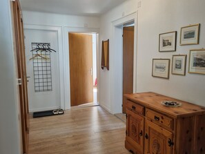 Ein Flur mit Holzdielen, einem Garderobenschrank, einer Holzkommode und gerahmten Bildern an der Wand.