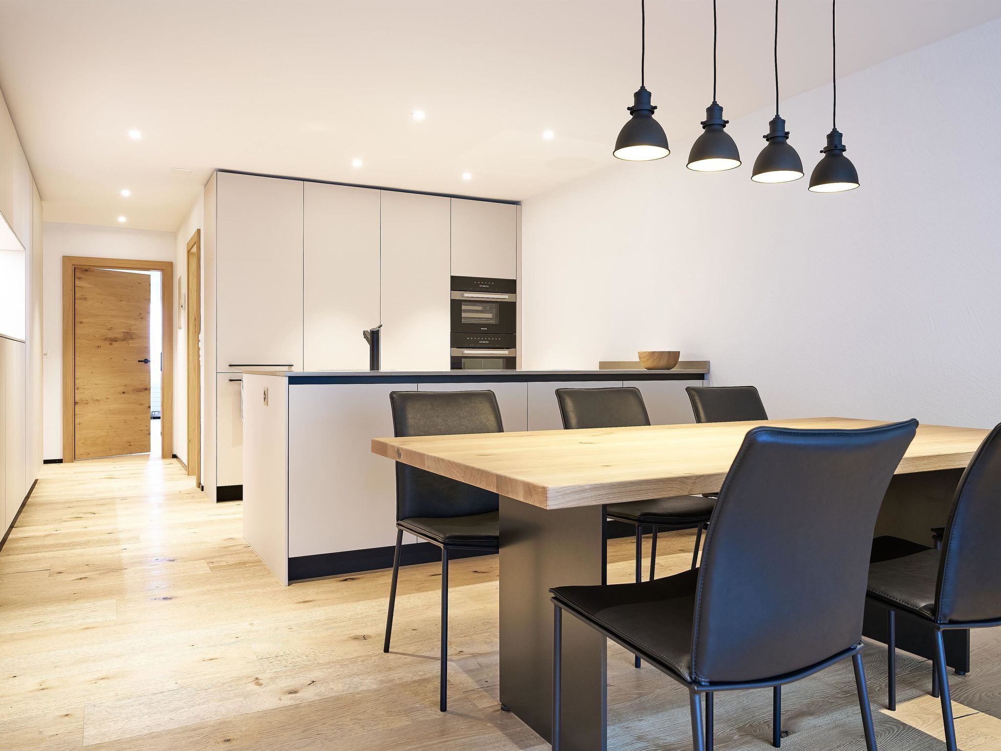 Une cuisine moderne avec des meubles blancs, une table à manger en bois et des chaises noires.