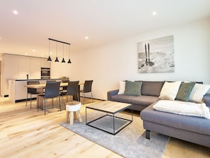 Ein modernes Wohnzimmer mit einer grauen Couch, einem Couchtisch und einem Essbereich mit Stühlen und Tisch.