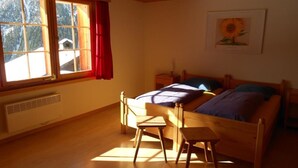 Ein Schlafzimmer mit Bett, Stuhl, Nachttisch, Fenster mit Vorhängen und einem Wandbild.