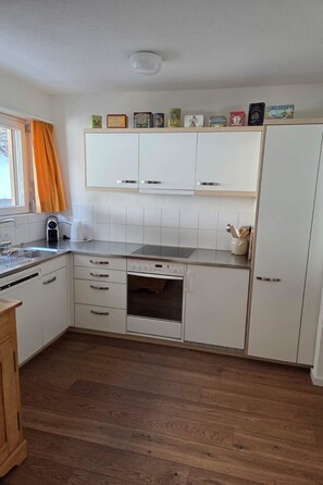 Eine kompakte Küche mit weißen Schränken, einem Einbauofen, einer Spüle und einem Fenster mit Vorhängen.