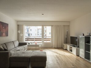 Una sala moderna con sofá, reposapiés, televisor y un mueble de vidrio.