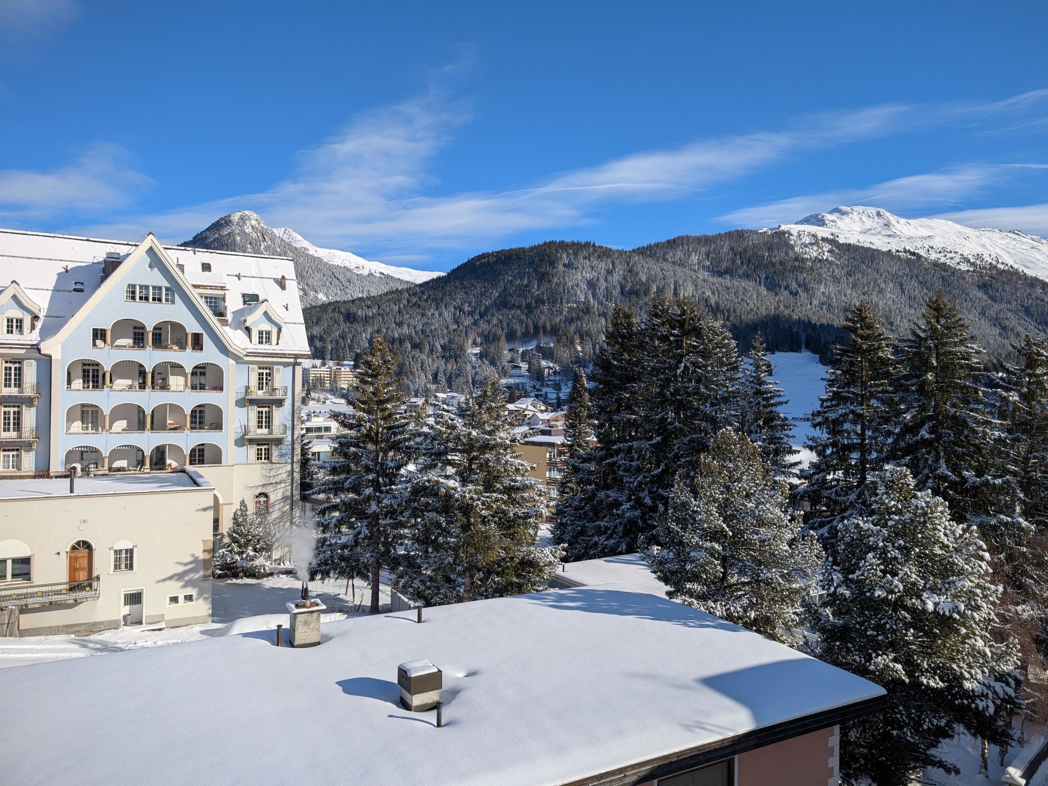 Un paysage de montagne enneigé, avec un bâtiment doté de nombreux balcons et d’un toit recouvert de neige.