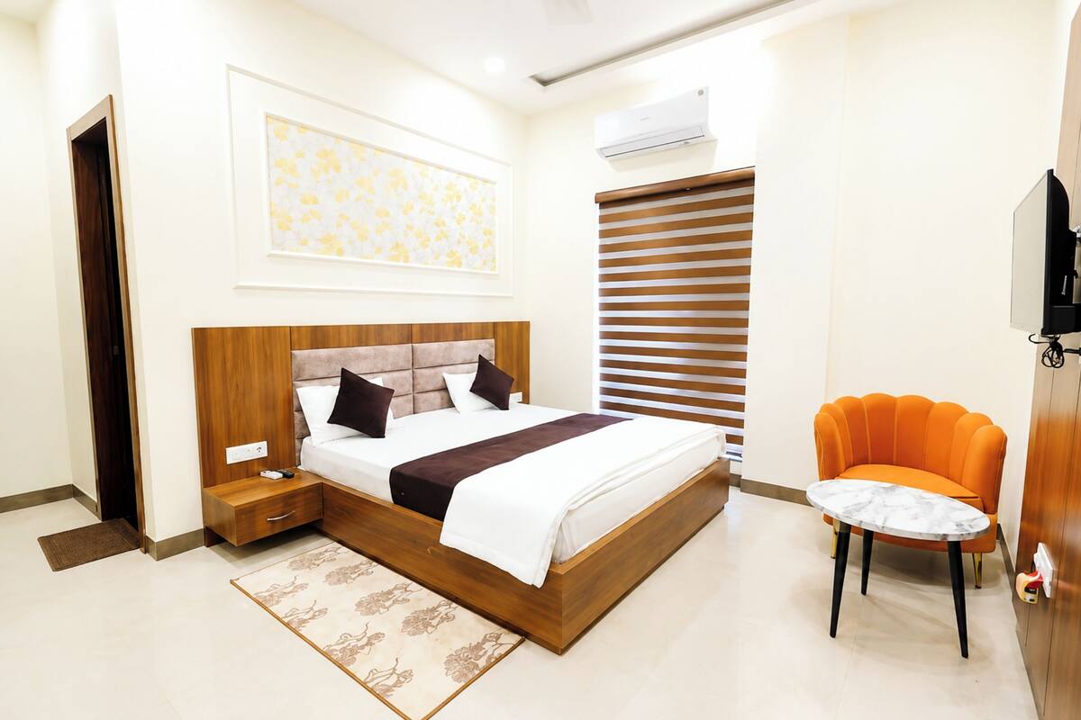 A modern bedroom with a wooden bed, a bedside table, a small round table, a sofa, and a television.