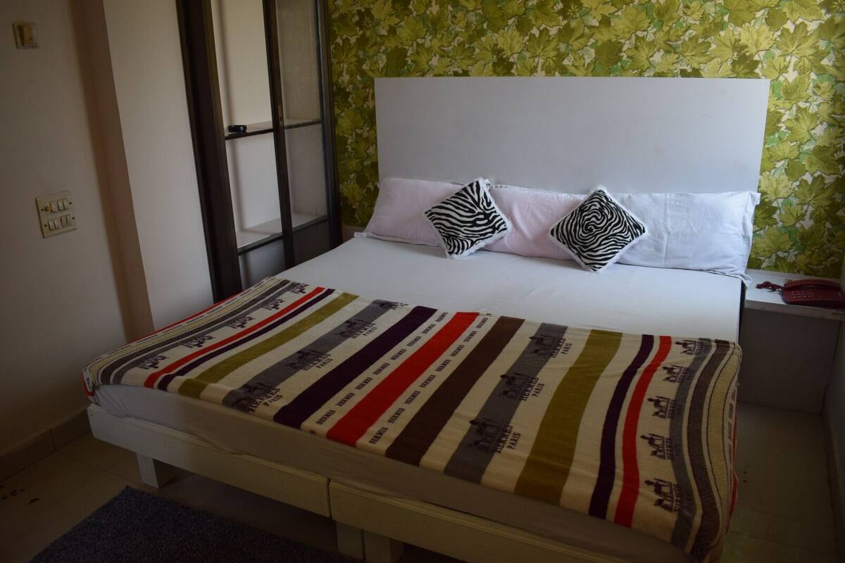 Una cama con ropa de cama a rayas, dos almohadas, una mesita de noche con un teléfono y una ventana con vistas.