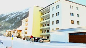 Un edificio de varios pisos con balcones, una zona de estacionamiento y una calle cubierta de nieve.