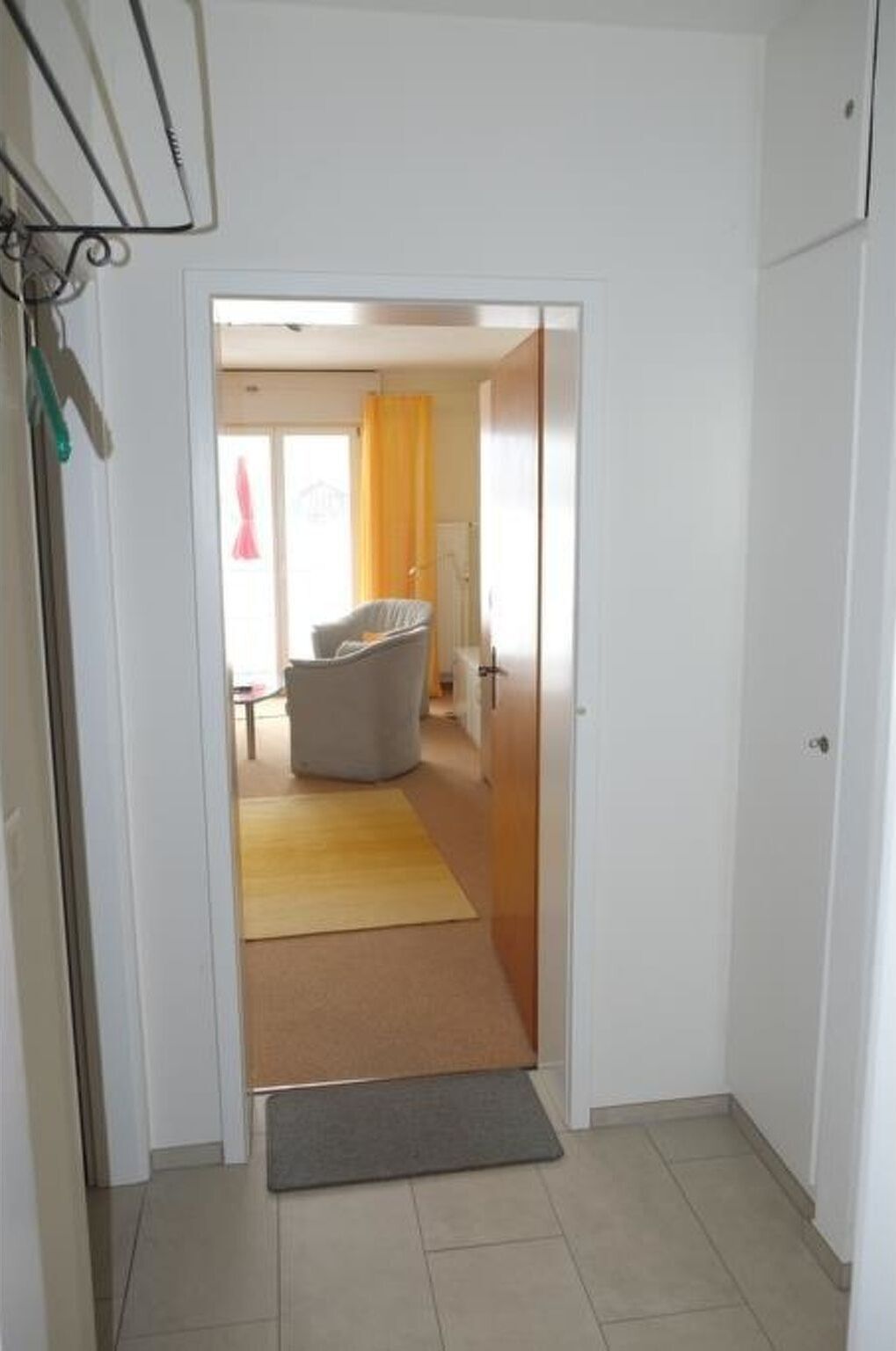 A hallway leading to a room with a chair and a yellow rug.