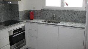 Une cuisine dotée de plans de travail en granit, d’appareils électroménagers en acier inoxydable, d’une machine à café rouge et d’une fenêtre offrant une vue agréable.