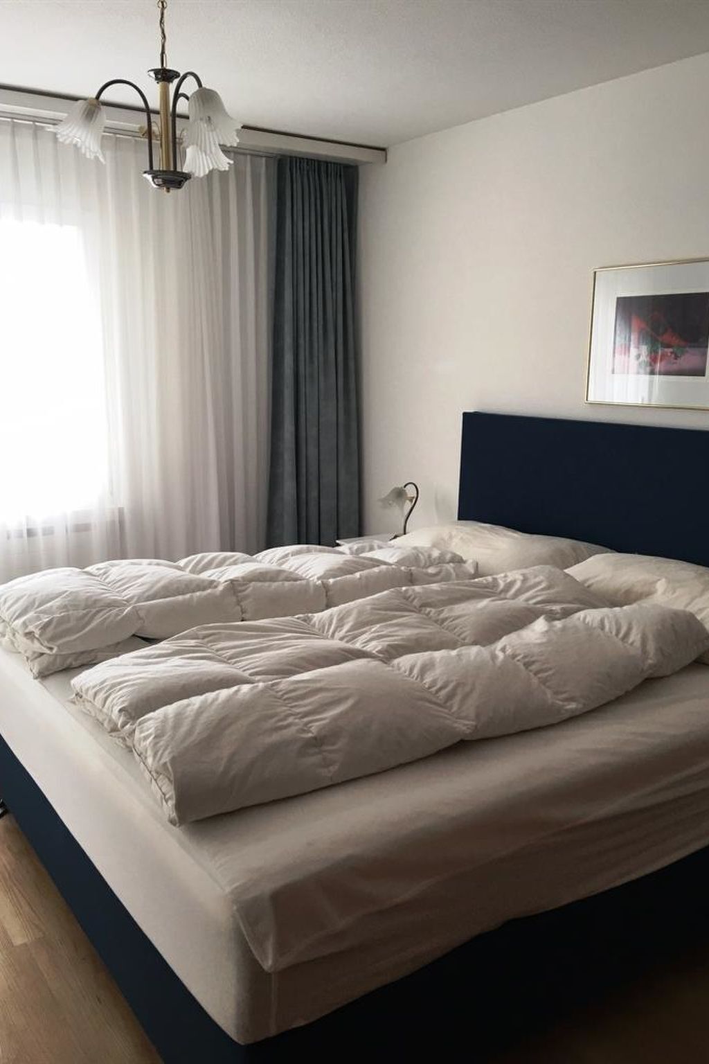 A neatly made bed in a room with a dark headboard, a hanging light fixture, and a framed picture on the wall.