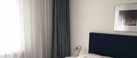A neatly made bed in a room with a dark headboard, a hanging light fixture, and a framed picture on the wall.