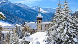 Een bergstad bedekt met sneeuw, met een opvallende kerktoren, omgeven door sneeuwzware bomen en gebouwen.