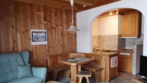 Een gezellige kamer met een bank, een houten eettafel en een keukenhoek met houten kasten en een fornuis.