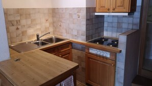 Een keuken met een spoelbak, fornuis, houten kastjes en een aanrecht.