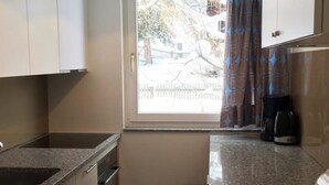 Cocina compacta con ventana, cafetera y un taburete pequeño.
