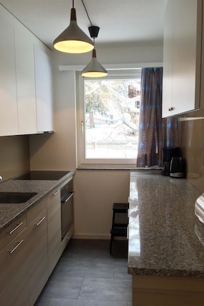 Cocina compacta con ventana, cafetera y un taburete pequeño.