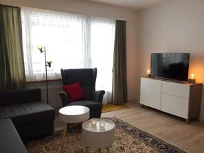 Una sala de estar con sofá, sillón, televisor y una mesita con velas.