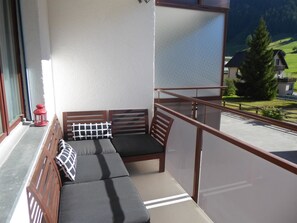 Un balcón con zona de estar acolchada, un farol rojo y vistas a un paisaje verde con casas.