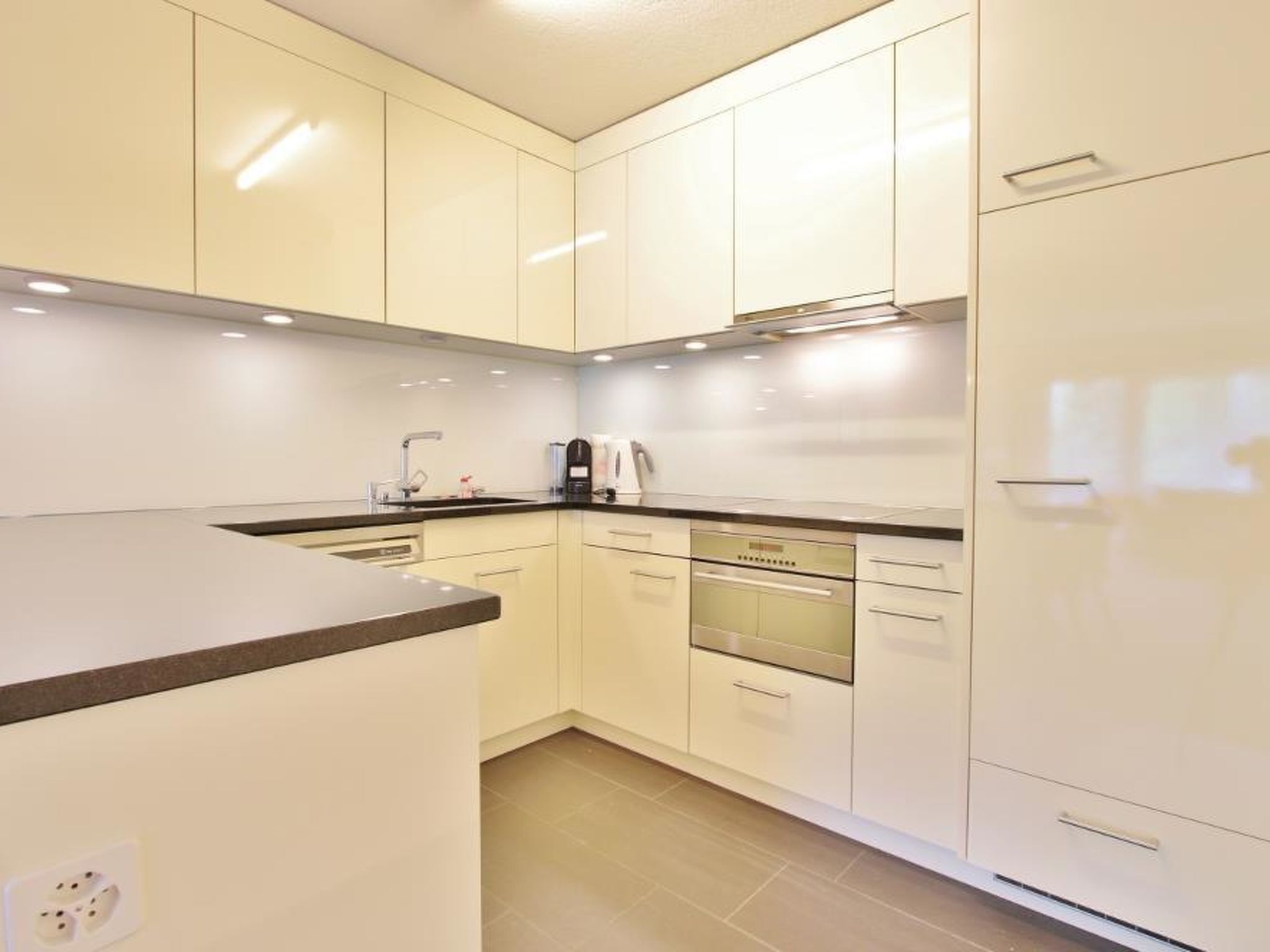Una cocina moderna con armarios blancos, horno empotrado y cafetera.