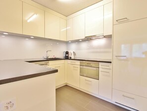 Una cuina moderna amb armaris blancs, forn integrat i cafetera.