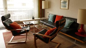 Una sala de estar con un sofá, dos sillones, una mesa de centro de vidrio y una lámpara roja.