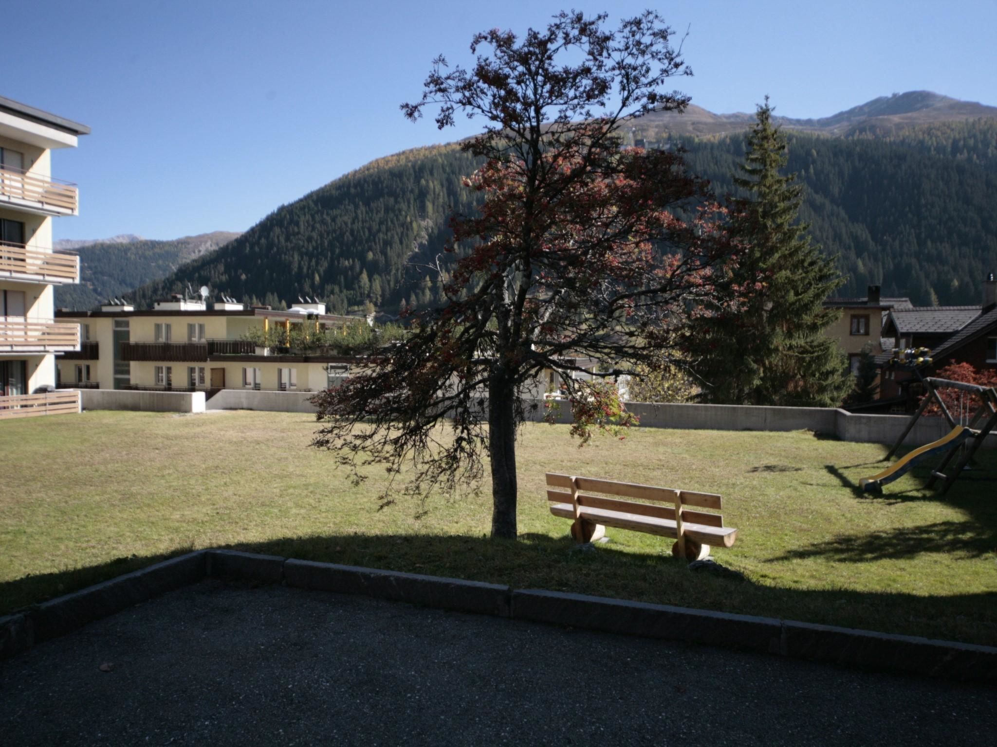 A grassy area with a bench, a playground, and buildings in the background.