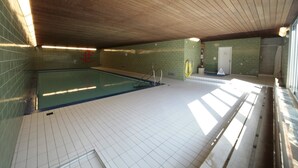 Una piscina interior con techo de madera, paredes y piso azulejados.