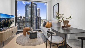 A modern living room with a large window, a sofa, a dining table, and a television. - Bright Apt Southbank Near Crown Casino ,pool &gym (Melbourne)