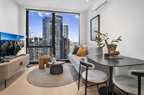 A modern living room with a large window, a sofa, a dining table, and a television. - Bright Apt Southbank Near Crown Casino ,pool &gym (Melbourne)