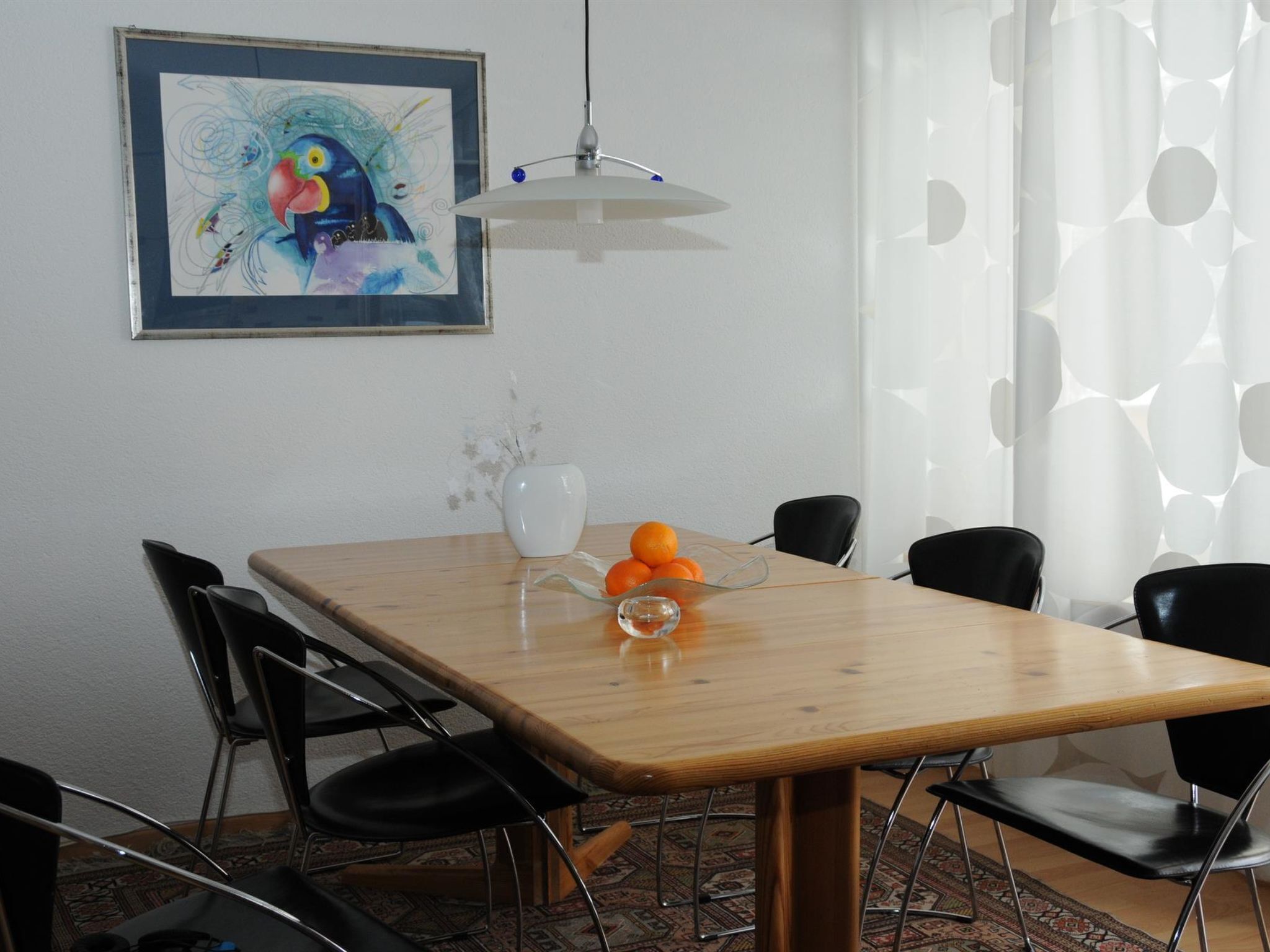 Ein Essbereich mit einem Holztisch, schwarzen Stühlen, einer weißen Vase und einem Gemälde an der Wand.