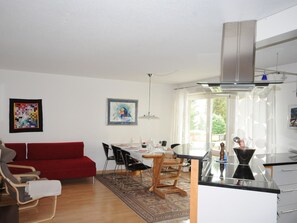 Ein modernes Wohnzimmer mit einem roten Sofa, einem Essbereich mit Stühlen, einer Küche mit Herd und Kunstwerken an den Wänden.
