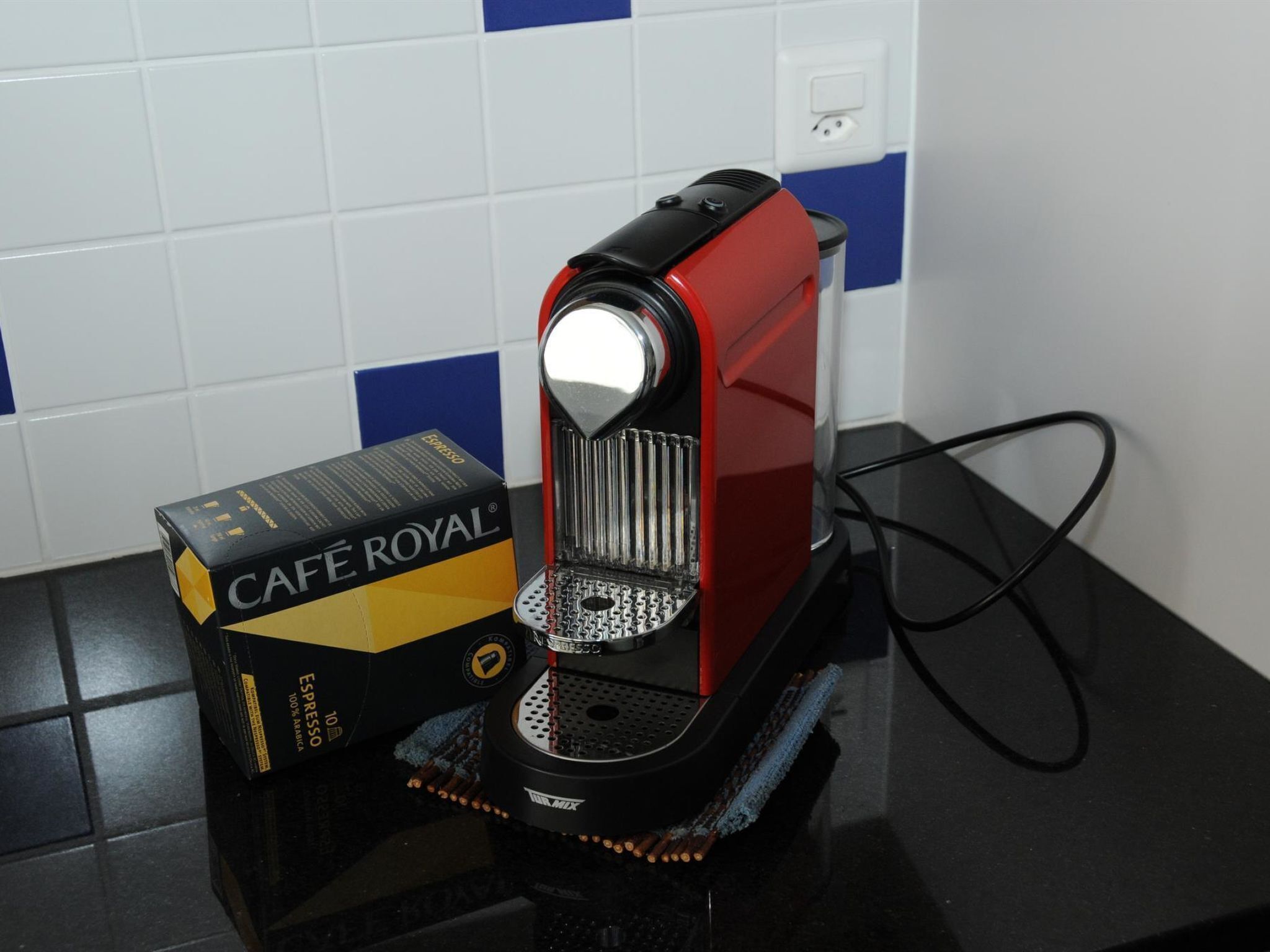 Máquina de café com corpo vermelho e preto, porta-cápsulas e cabo de alimentação conectado.
