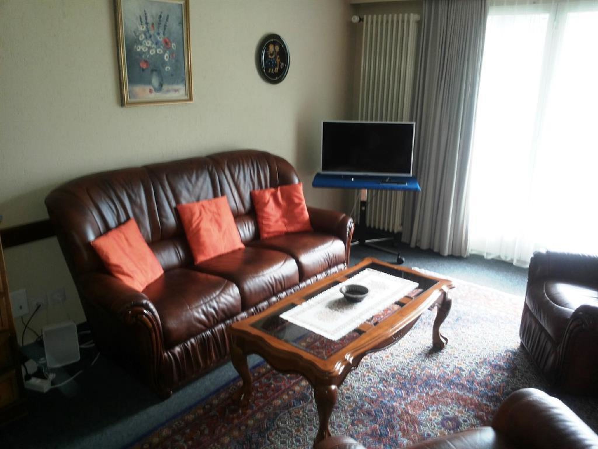 Ein Wohnzimmer mit einem braunen Ledersofa, einem Holztisch, einem Flachbildfernseher und einem gemusterten Teppich.
