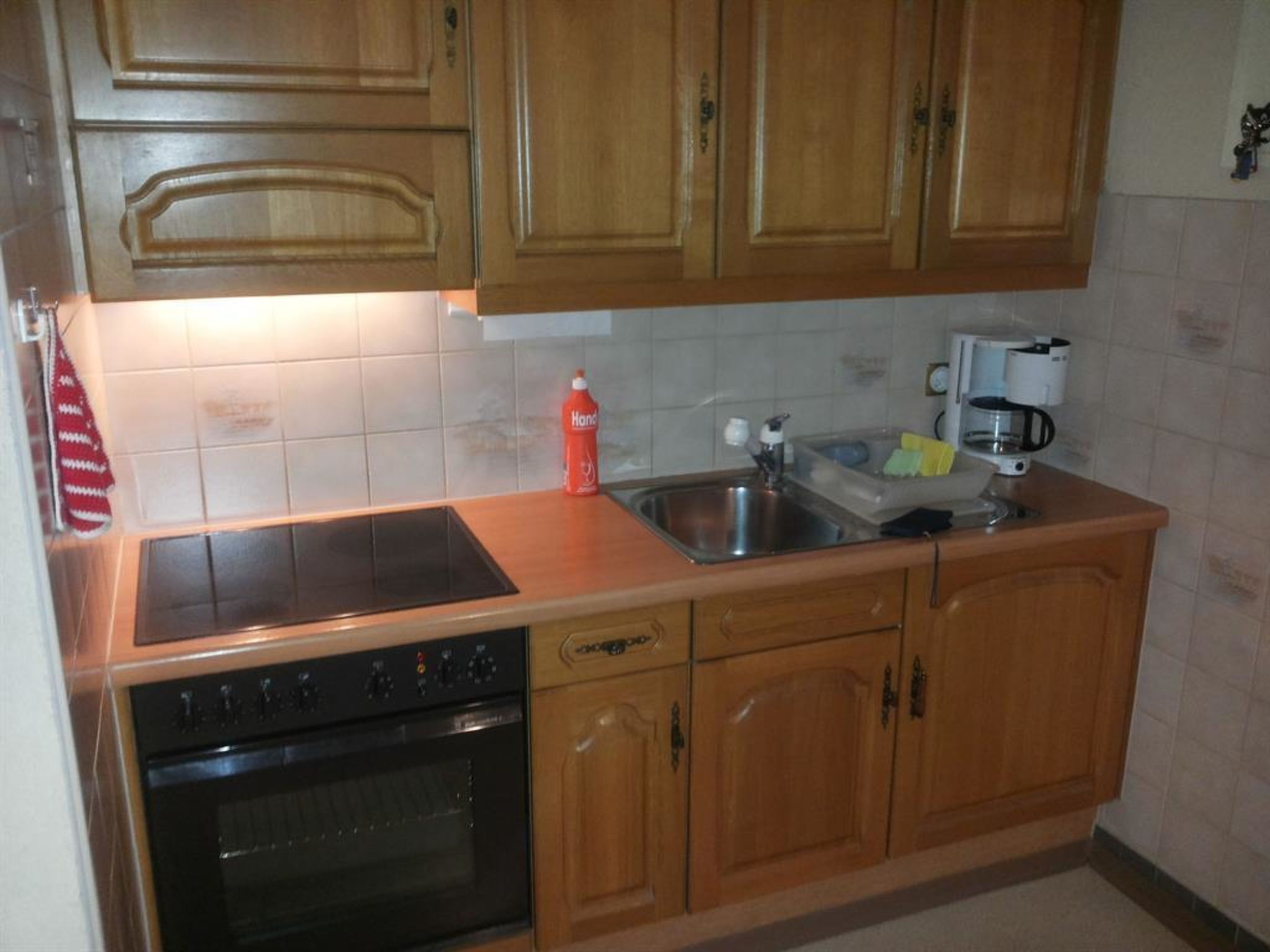 A kitchen with wooden cabinets, a stainless steel sink, a coffee maker, and a red bottle.