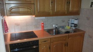 A kitchen with wooden cabinets, a stainless steel sink, a coffee maker, and a red bottle. - Golfpark B 14 Appartement/Fewo, Dusche oder Bad, WC 1½-Zimmerwohnung by Interhome (Davos)